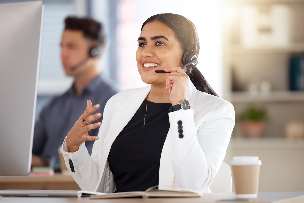 Woman, call center and computer with headset consulting in telemarketing, customer service or support at office. Happy female consultant talking on mic sitting by desktop PC in contact us for sales.