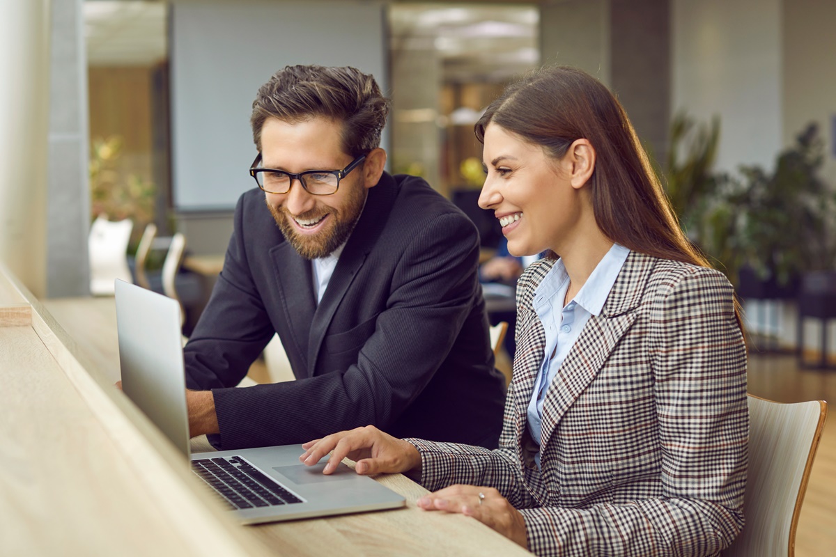 Company employees working at same desk in a modern office looking at laptop monitor screen.