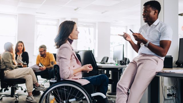 A businesswoman who uses a wheelchair is discussing project and brainstorming whit multicultural colleague at enterprise. A multicultural businesspeople debating about new assignment at office.