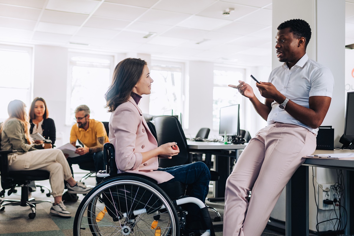 A businesswoman who uses a wheelchair is discussing project and brainstorming whit multicultural colleague at enterprise. A multicultural businesspeople debating about new assignment at office.