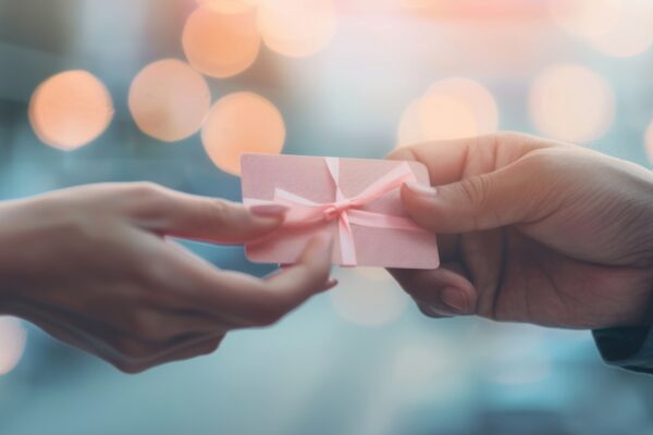 Two hands are in the act of exchanging a gift card while shopping in a busy retail environment.