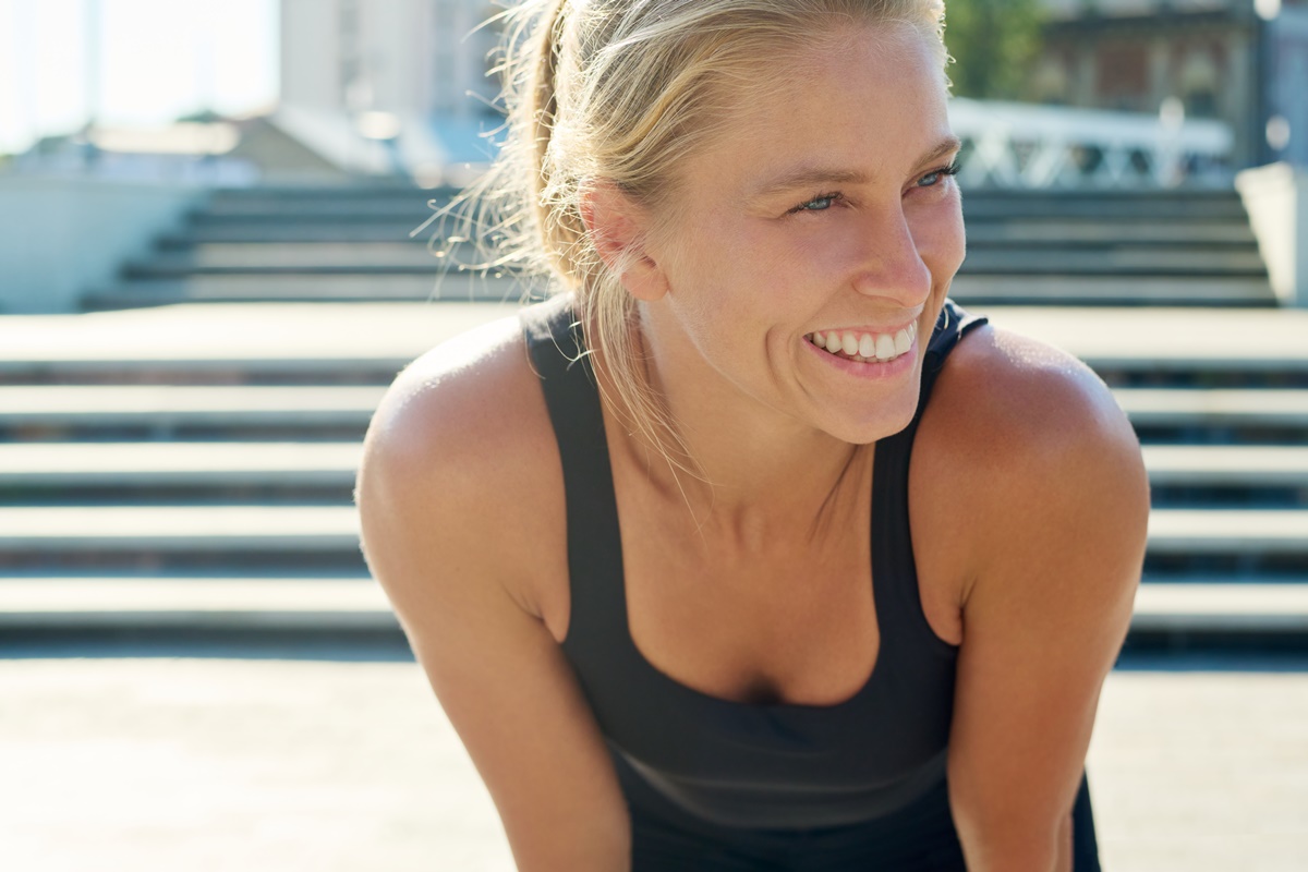 Young cheerful blond sportswoman in black activewear enjoying break after outdoor sports training while standing in front of camera