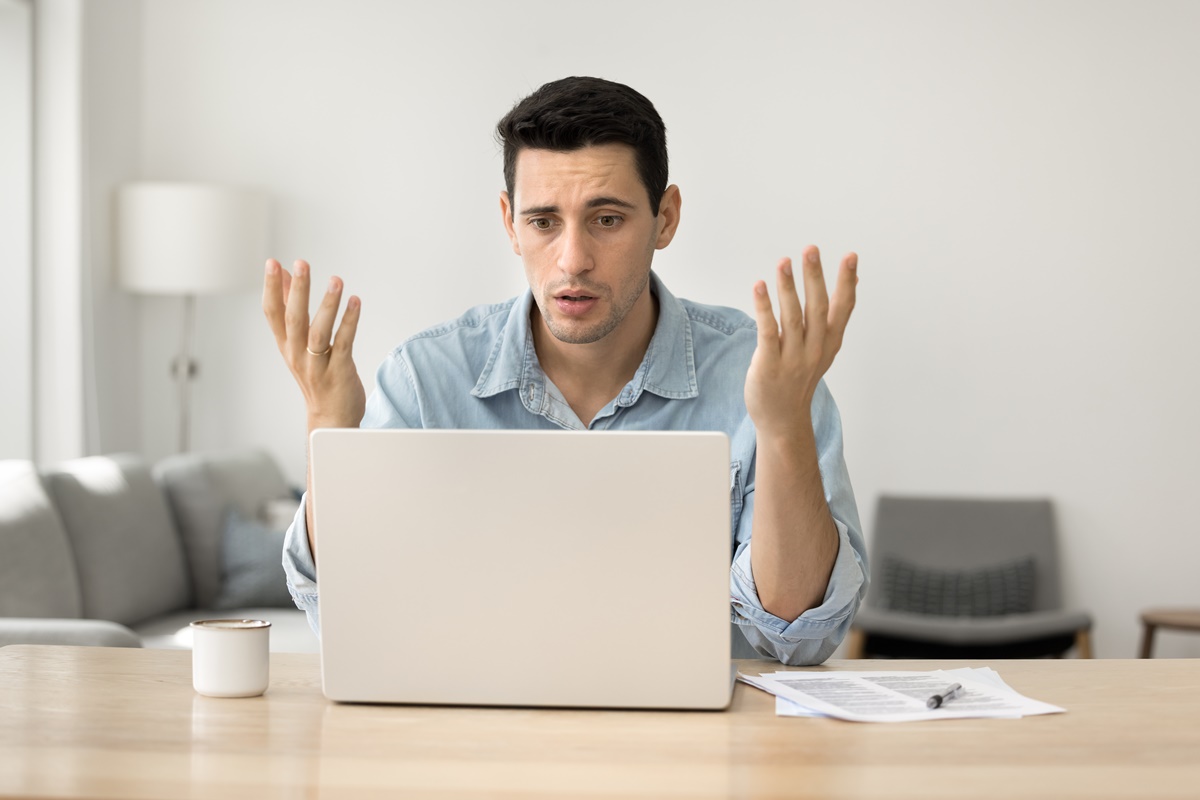 Concerned puzzled Latin freelance worker man looking at laptop with confused hand gesture. Frustrated worried computer user getting bad news, job technology failure, feeling shock, stress.