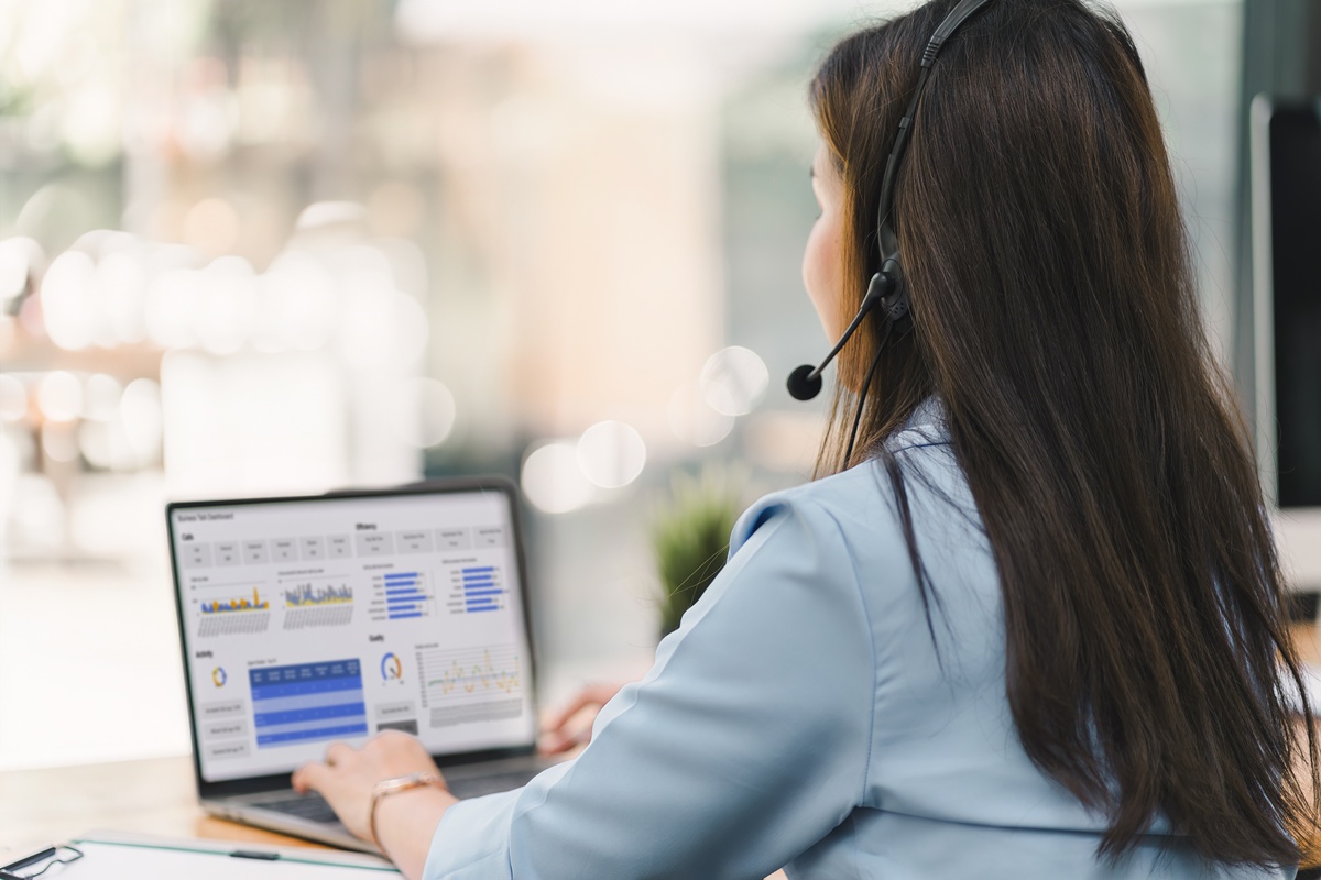 Operator wearing a headset, using a dashboard on laptop for data analysis in modern office